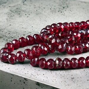 May include: A strand of deep red faceted glass beads. The beads are arranged in a circular pattern and have a slight iridescent sheen.