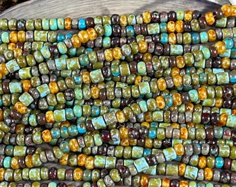May include: A close-up of a strand of small, colorful glass beads. The beads are a mix of brown, green, yellow, and blue. The beads are arranged in a random pattern.