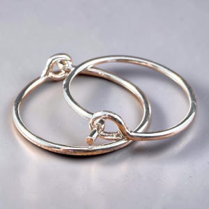 May include: A pair of silver-toned hoop earrings featuring a thin, circular wire design. Each earring has a simple hook-and-loop closure mechanism where the end of the wire loops through a small circular opening to secure the hoop in place.