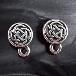 May include: Two silver-toned metal buttons with a Celtic knot design. Each button has a circular shape with a loop at the bottom. The buttons are displayed on a dark surface.