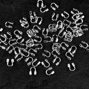 May include: A collection of small, silver-colored metal jewelry findings, including U-shaped clasps and connectors, scattered on a dark surface. These components are likely used in jewelry making or crafting projects.