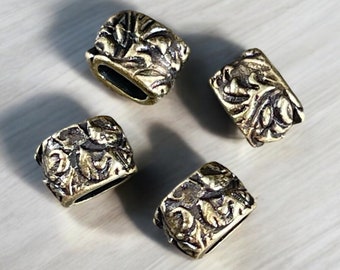 May include: Four antique brass-colored beads with a rectangular shape and intricate floral designs. The beads have a hollow center and are arranged on a light-colored surface. The detailed carvings give the beads a vintage aesthetic.