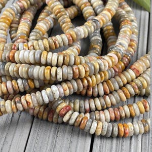 May include: Close-up of gemstone bead strands in beige, orange, and grey hues. The beads are round with a flattened profile. Strung together, they create a textured, organic appearance. These beads are likely used for jewellery making, with each bead measuring approximately 0.5 cm in diameter.