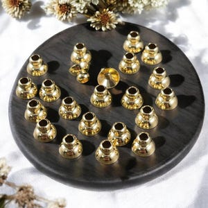 May include: A set of 30 gold-colored metal bottle stoppers. The stoppers are shaped like a dome with a small hole in the center. They are arranged in a circle on a dark wooden surface.