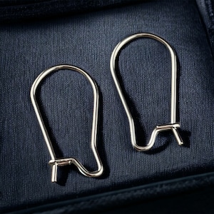 May include: A pair of silver earring hooks, made of metal, with a simple, curved design. The hooks are shown against a dark blue background.