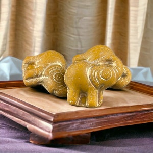 May include: Two small, yellow ceramic elephant figurines with intricate details on a wooden tray.