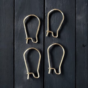 May include: Four gold-colored earring hooks, also known as ear wires, are displayed against a black wooden background.