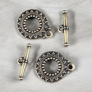 May include: Four antique brass toggle clasps. Two circular clasps with a detailed border and two bar clasps. The clasps are designed with a vintage aesthetic, featuring intricate patterns and a warm, aged finish.