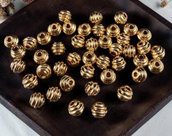 May include: A collection of gold-colored, spiral-grooved beads. The beads are round with a hole through the center, and are displayed on a dark wooden tray. The beads are likely for jewelry making or other crafts.