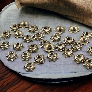 May include: A collection of gold-toned metal embellishments with a decorative, scalloped design. The embellishments are arranged on a blue fabric surface.