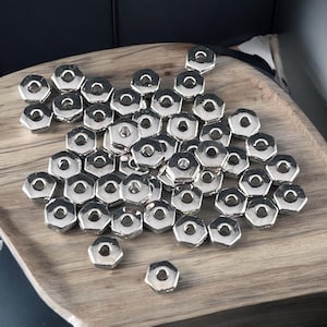 May include: A large pile of silver-colored metal hex nuts on a wooden surface.