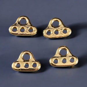 May include: Four gold-colored metal rings with three holes each. The rings are shaped like a UFO or flying saucer.