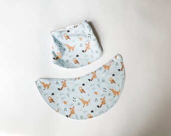 May include: Two light blue baby bibs with a pattern of foxes, owls, and leaves. The bibs have white snaps.