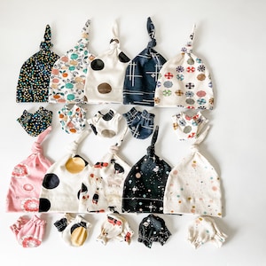 May include: A set of 10 baby hats and matching mittens in various patterns, including polka dots, geometric designs, and floral prints. The hats are made of soft, breathable fabric and are perfect for keeping baby's head warm and cosy.
