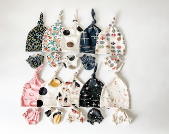 May include: A set of 10 baby hats and matching mittens in various patterns, including polka dots, geometric designs, and floral prints. The hats are made of soft, breathable fabric and are perfect for keeping baby's head warm and cozy.