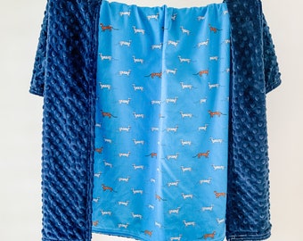 Puede incluir: Una manta para bebé azul y blanca con un patrón de perros. La manta está hecha de tela suave y afelpada, perfecta para acurrucarse.