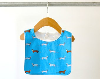May include: A blue baby bib with a white and brown animal print. The bib has a white snap closure at the neck.