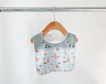 May include: A light blue and white baby bib with a woodland animal print featuring owls, foxes, and leaves. The bib has a white, soft, absorbent layer on the back.