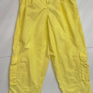 Puede incluir: Pantalones cargo de color amarillo brillante con dos bolsillos laterales y cierre de bot&oacute;n. Los pantalones est&aacute;n hechos de una tela ligera y tienen un ajuste relajado. Los pantalones son de color liso y parecen nuevos.