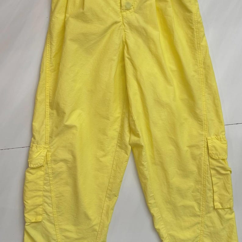 Puede incluir: Pantalones cargo de color amarillo brillante con dos bolsillos laterales y cierre de bot&oacute;n. Los pantalones est&aacute;n hechos de una tela ligera y tienen un ajuste relajado. Los pantalones son de color liso y parecen nuevos.
