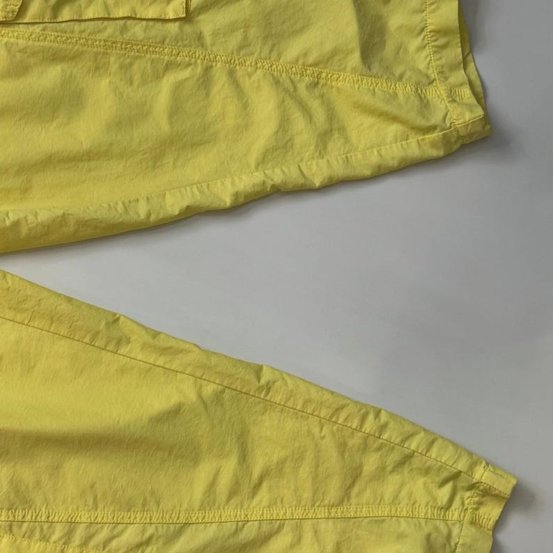Puede incluir: Primer plano de unos pantalones de color amarillo brillante. La tela parece ligera y ligeramente texturizada, con costuras y pespuntes visibles. Los pantalones est&aacute;n doblados, mostrando los detalles de los bolsillos y el dise&ntilde;o general. El color es un amarillo vibrante y soleado.