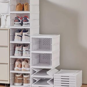 May include: White plastic shoe storage containers with clear front panels. Several pairs of shoes are visible inside the containers. The containers are stacked in a vertical arrangement, with some boxes open and others closed.