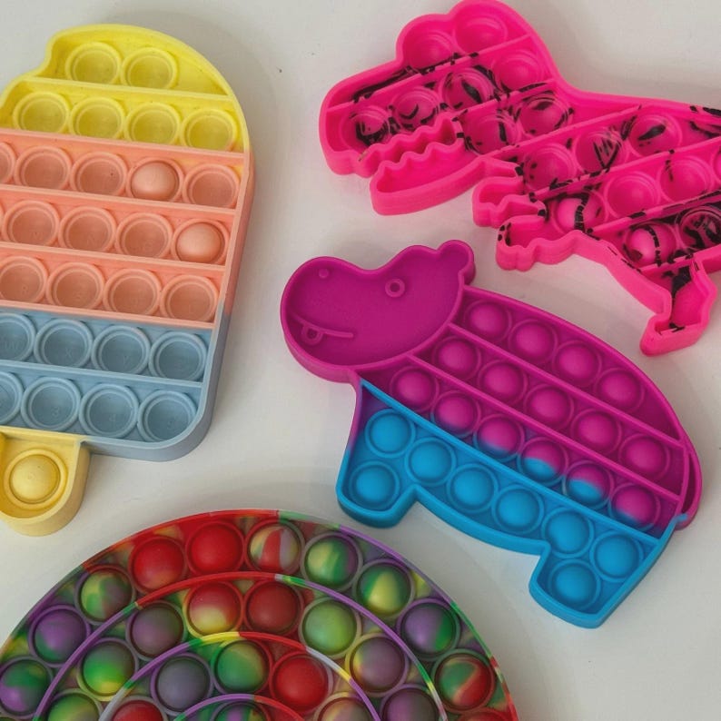 Puede incluir: Una colecci&oacute;n de coloridos juguetes sensoriales de silicona en varias formas. Incluye un helado, un dinosaurio, un hipop&oacute;tamo y un arco&iacute;ris. Los juguetes presentan m&uacute;ltiples depresiones en forma de burbujas que se pueden empujar hacia adentro y hacia afuera.