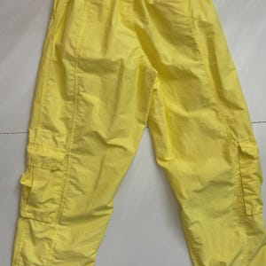 Puede incluir: Pantalones cargo de color amarillo brillante con m&uacute;ltiples bolsillos y cintura con cord&oacute;n. Los pantalones est&aacute;n hechos de un material ligero y tienen detalles de costura visibles. El estilo casual es adecuado para el uso diario.