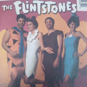 May include: A McCall's sewing pattern envelope for The Flintstones costumes. The cover displays four outfits: an orange tunic with black triangles and a blue tie, a white strapless dress with a white bead necklace, a brown tunic, and a blue dress.