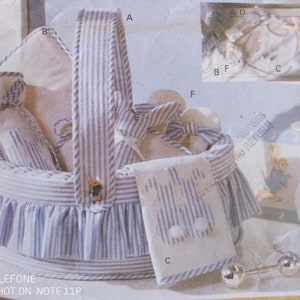 May include: A round basket with a blue and white striped fabric cover and a ruffled skirt. The basket contains several fabric items labeled with letters A through F, including a small bag, a rectangular cloth, and a rabbit-shaped ornament.