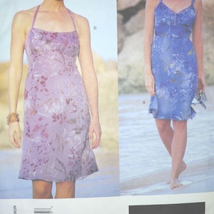 May include: A sewing pattern envelope for Anna Sui design 2295, featuring two variations of a knee-length dress with floral prints. View B is a lavender halter-neck dress, and View A is a blue spaghetti-strap dress with a ruffled hemline.