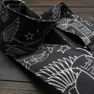 May include: Black guitar strap with white tattoo-style designs. The strap features images of a swallow, roses, stars, dice, and banners with the words "TRUE LOVE" and "LOVE". The strap has black leather ends and metal rivets.
