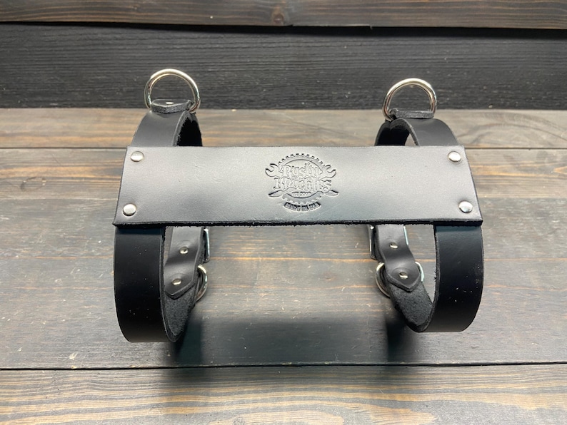 May include: Black leather bag carrier with silver metal rings and buckles. The carrier has a stamped logo that reads "Austin, Texas, USA". The carrier is designed to hold a bag or other items.