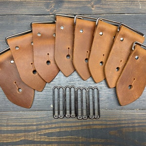 May include: Eight brown leather straps with silver buckles and eight silver metal loops. The straps are arranged in a semi-circle with the loops in the center.