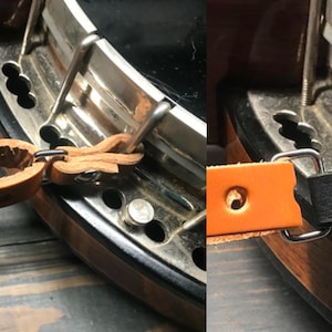 May include: Close-up of a banjo's metal and wood components. The image shows leather straps attached to the banjo's metal hardware. The banjo has a wooden rim and a shiny metal body.