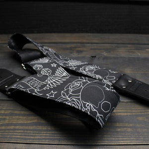 May include: Black guitar strap with a white tattoo-style design featuring skulls, roses, dice, and the word "LOVE". The strap is made of a durable material and has black leather ends.