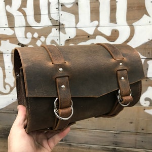 May include: A brown leather motorcycle saddlebag with silver buckles and straps.