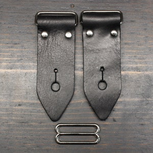 May include: Two black leather guitar strap end pieces with silver metal buckles and a silver metal strap adjuster.