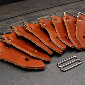 May include: Seven brown leather strap ends with silver metal buckles, and one silver metal buckle. The strap ends are arranged in a fan shape, with the buckles facing outward.