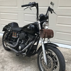 May include: A black Harley Davidson motorcycle with a brown leather saddlebag. The motorcycle has a chrome front fender and a chrome exhaust pipe.