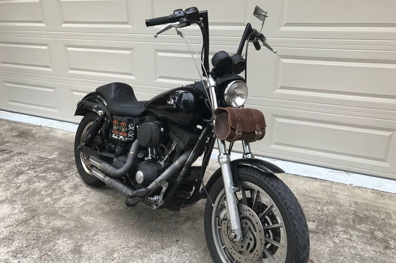 May include: A black Harley Davidson motorcycle with a brown leather saddlebag. The motorcycle has a chrome front fender and a chrome exhaust pipe.
