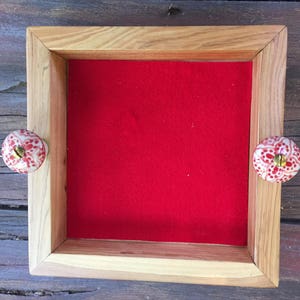 May include: A wooden tray with a red velvet lining and two decorative knobs with white and red floral patterns.