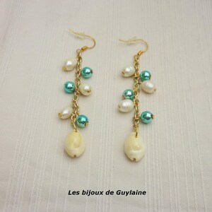 Puede incluir: Un par de pendientes colgantes con cadenas doradas, cuentas blancas y turquesas, y un dije en forma de concha de color crema. Los pendientes se exhiben sobre una superficie blanca. Texto en la parte inferior: "Les bijoux de Guylaine".