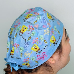 May include: Light blue scrub cap featuring cartoon characters SpongeBob SquarePants and Squidward, along with the phrase "Not Today." The cap has a tie closure and is decorated with flowers and starfish.