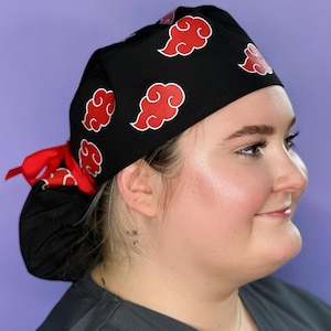 Puede incluir: Un gorro de quirófano negro con diseños de nubes rojas. El gorro tiene una cinta roja que se puede atar en la parte posterior de la cabeza.