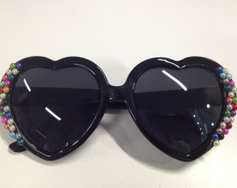 May include: Black heart-shaped sunglasses with a rainbow of small beads around the edges of the frames.