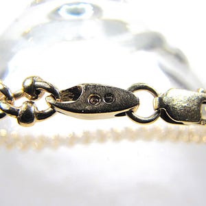 May include: Close-up of a gold-colored bracelet with a decorative chain design. The bracelet features a secure clasp and is displayed against a blurred background. The jewelry piece is likely made of gold.