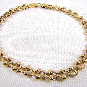 May include: A gold-colored bracelet with a delicate, linked design. The bracelet features a series of small, rounded links connected to form a flexible chain. The clasp is also gold-toned. The bracelet is displayed on a white surface.