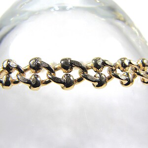 May include: A gold-colored bracelet with a chain-link design. The links are oval-shaped and connected in a repeating pattern. The bracelet is displayed against a blurred, light background.