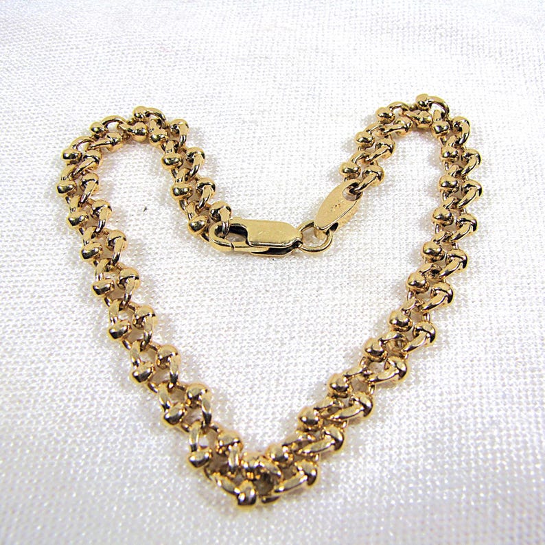 May include: A gold-colored bracelet with a unique chain design. The bracelet is made of small, rounded links connected together. The clasp is a simple, secure design. The bracelet is displayed on a white surface.